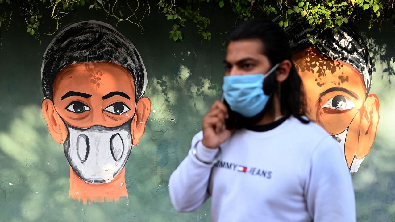 A man wearing a facemask as a preventive measure against the Covid-19 coronavirus speaks on his mobile phone while walking past a mural along a roadside in New Delhi on February 24, 2021. Credit: AFP Photo