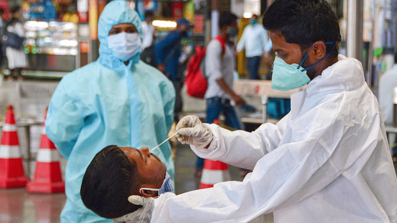 A health worker takes a nasal swab sample of a passenger for coronavirus tests. Credit: PTI Photo