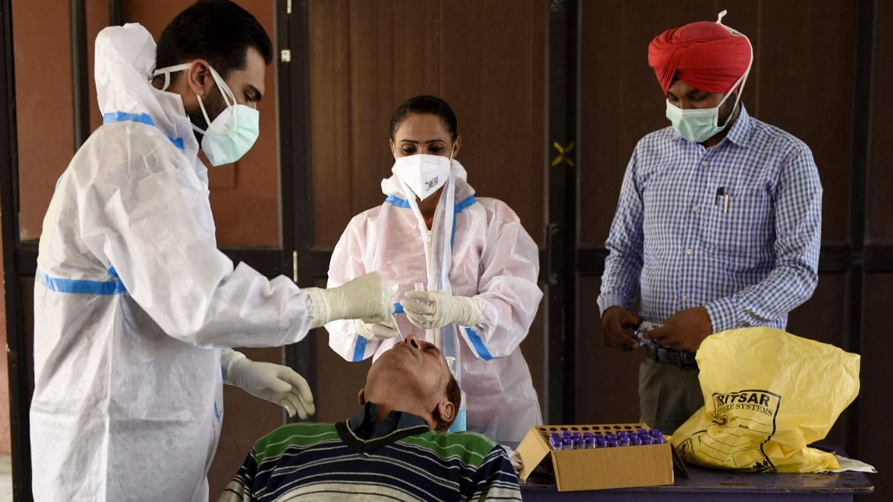 A health worker (L) collects a nasal swab sample from a teacher to test for the Covid-19 coronavirus at a school in Amritsar on February 26, 2021. Credit: AFP Photo