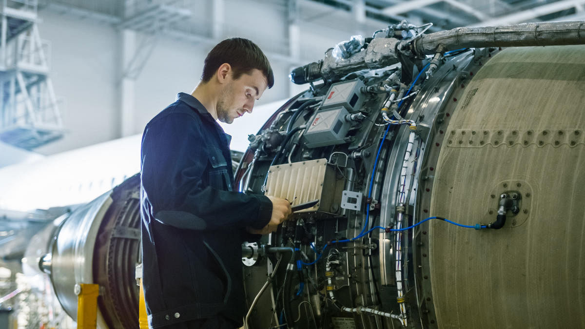 Aircraft Maintenance Mechanic Inspecting and Working on Airplane Jet Engine in Hangar