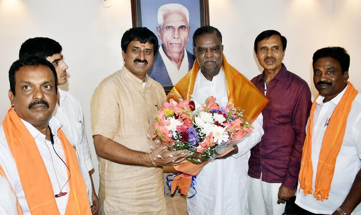 Tourism Minister C P Yogeeshwara greets Chamarajanagar MP V Srinivas Prasad in Mysuru on Tuesday. MUDA former chairman C Basavegowda is seen. DH Photo