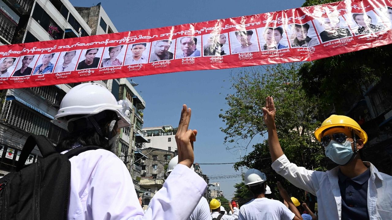 Medical personnel and students hold up the three finger salute below a row of portraits of people who died from security forces gun fire during a demonstration against the military coup in Yangon on March 5, 2021. Credit: AFP Photo