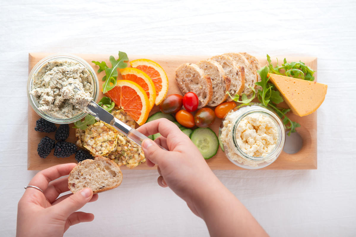 Personal perspective. Vegan boursin, feta and cheddar cheese in recycled jars. Raw fruit, berries, vegetables, whole grain bread and crackers on handmade reclaimed wood serving board.Cheese. Credit: Getty Images 