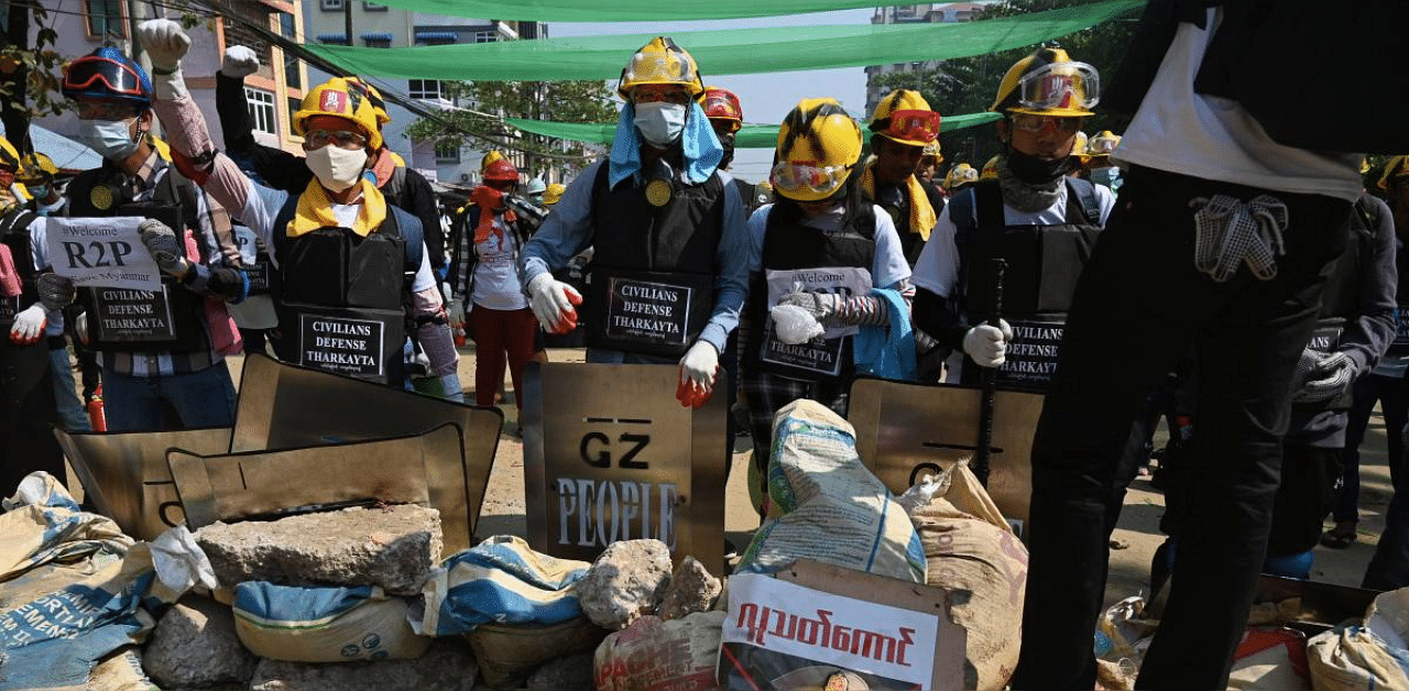 Protesters wearing hard hats stand by a blockade across a road during a demonstration against the military coup in Yangon. Credit: AFO photo. 