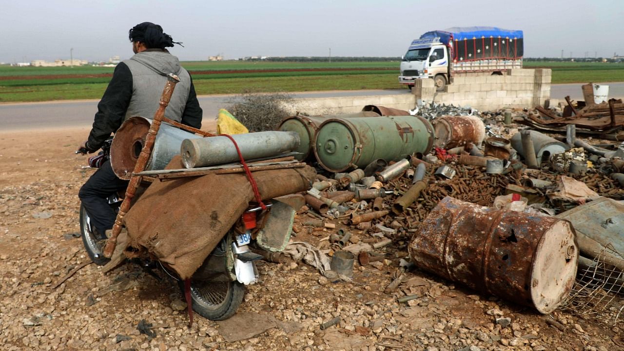 A Syrian man transports metal scraps including a shell casing on his motorcycle and he leaves a scrapyard on the outskirts of Maaret Misrin town in the northwestern Idlib province, on March 10, 2021. Credit: AFP Photo
