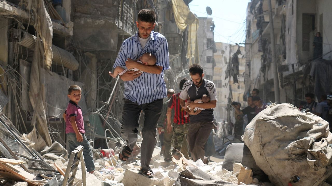 Syrian men carrying babies make their way through the rubble of destroyed buildings following a reported air strike, in 2017, at Aleppo, Syria. Credit: AFP File Photo