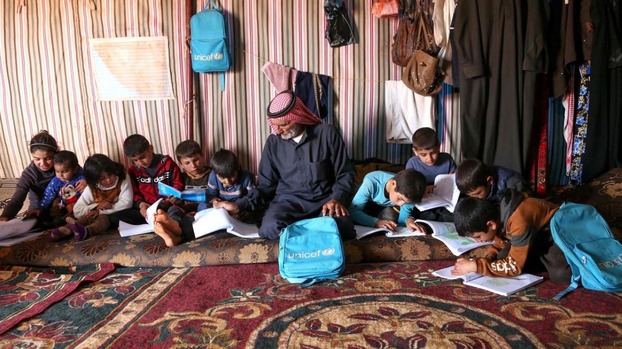 Abdel Razzak al-Khatoun helps his 11 orphaned grandchildren with their school work, inside a tent in an encampment in the village of Harbanoush, in the northern countryside of Syria's northwestern province of Idlib. Credit: AFP.