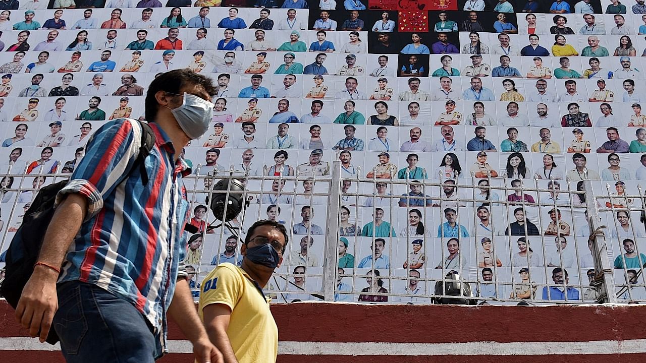 Pedestrians walk past a wall with pictures of Covid-19 coronavirus frontline workers displayed along the roadside to honour them, in Mumbai on March 15, 2021. Credit: AFP Photo