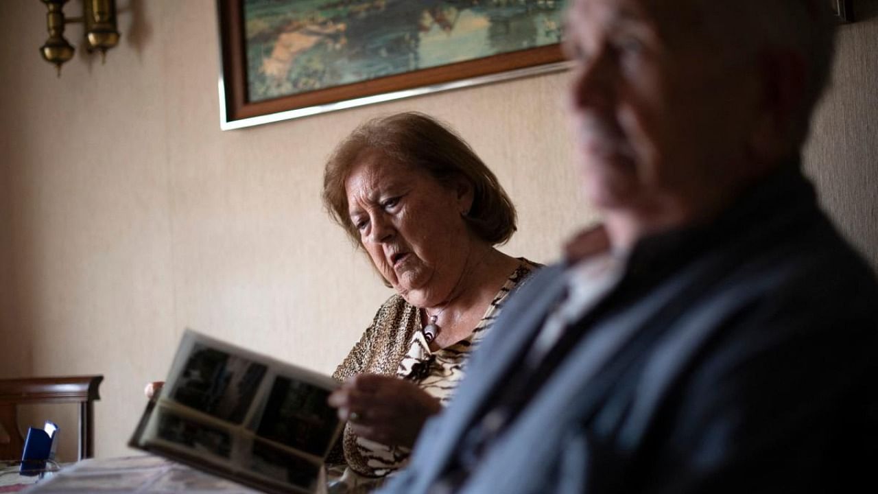 Jesus Blasco, 88 and suffering from throat cancer, looks at family photo albums with his wife Ana Maria Perez (L), 85, in their apartment in Barcelona on March 2, 2021. Credit: AFP.