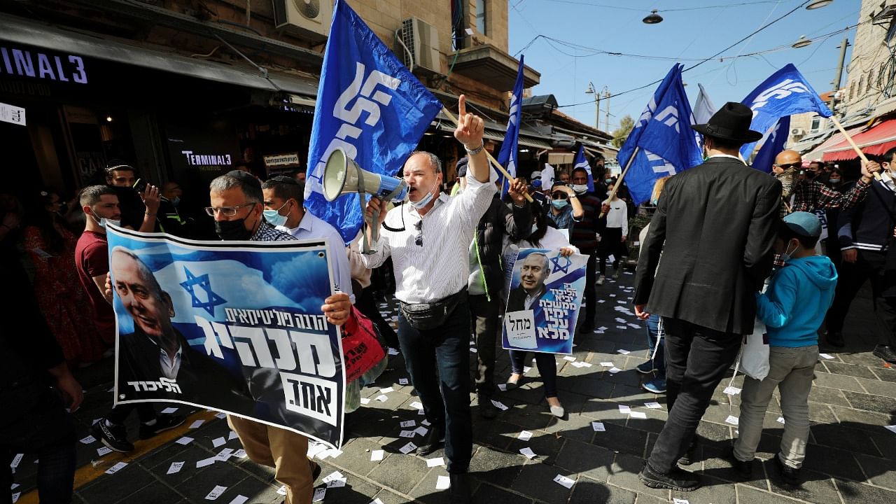 Supporters hold Likud party election campaign posters depicting it's leader, Israeli Prime Minister Benjamin Netanyahu and wave Likud flags, ahead of the March 23 general election, at Mahane Yehuda market in Jerusalem. Credit: Reuters Photo