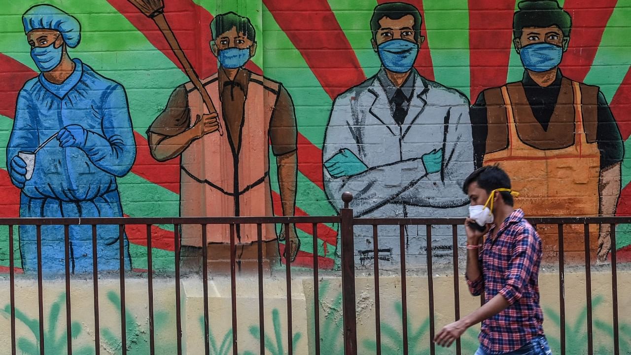 A pedestrian speaks on his mobile phone walking past a wall mural depicting frontline Covid-19 coronavirus warriors from various professions, in Mumbai on March 21, 2021. Credit: AFP Photo