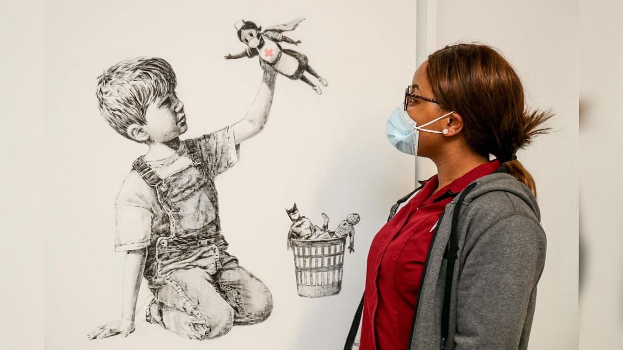 A handout picture received from University Hospital Southampton on May 7, 2020 shows a member of staff posing with an artwork by street artist Banksy called "Game Changer". Credit: AFP/University Hospital Southampton/Stuart Martin.