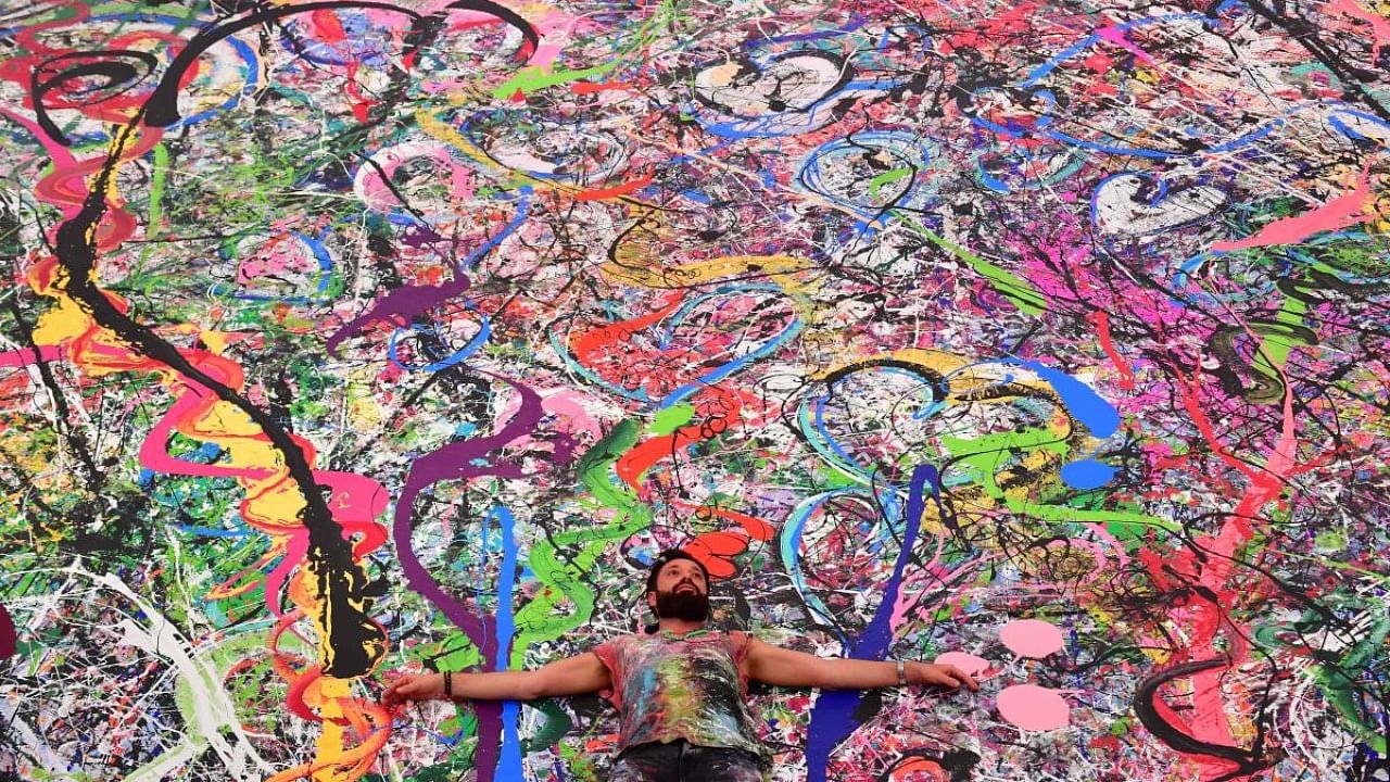 In this file photo taken on September 23, 2020 Contemporary British artist Sacha Jafri (C) lies on his record-breaking painting entitled 'The Journey of Humanity', in the Emirati city of Dubai. Credit: AFP