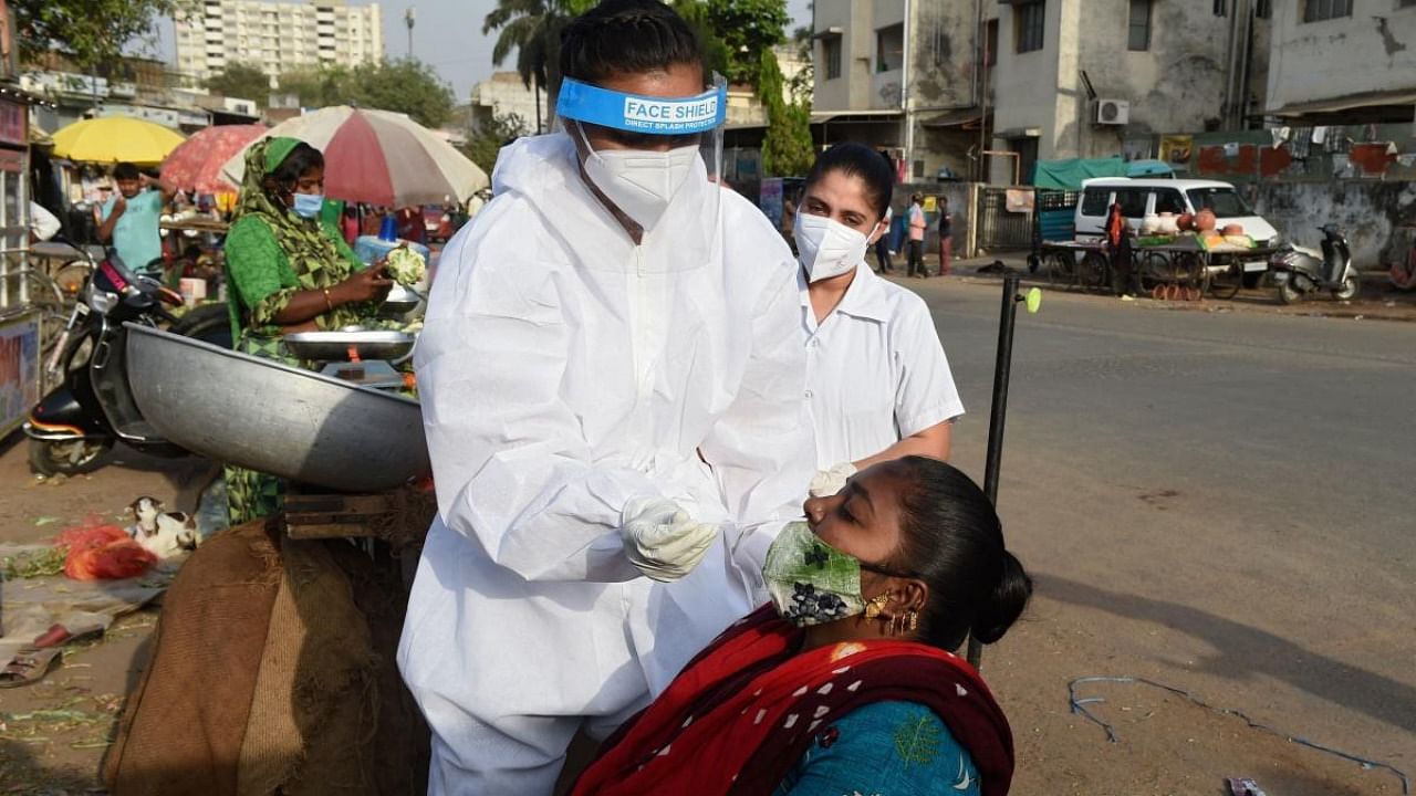 A health worker wearing protective gear collects a nasal swab sample from a woman to test for the Covid-19 coronavirus along the roadside vegetable market in Ahmedabad. Credit: AFP.