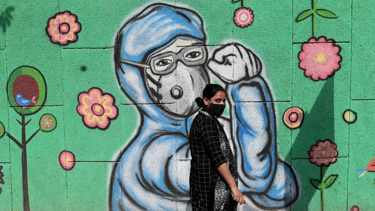 A pedestrian walks past a wall mural depicting frontline Covid-19 coronavirus warriors wearing face masks along a road in New Delhi on March 21, 2021. Credit: AFP Photo