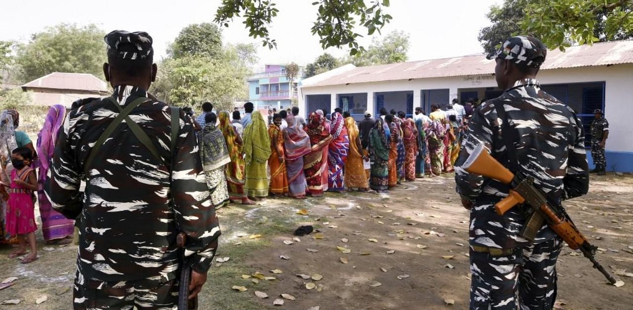 Paramilitary jawans guard as people wait in a queue to cast their votes at a polling station during the first phase of West Bengal Assembly elections, at Chandrapur in Lalgarh, Saturday, March 27, 2021. Credit: PTI Photo