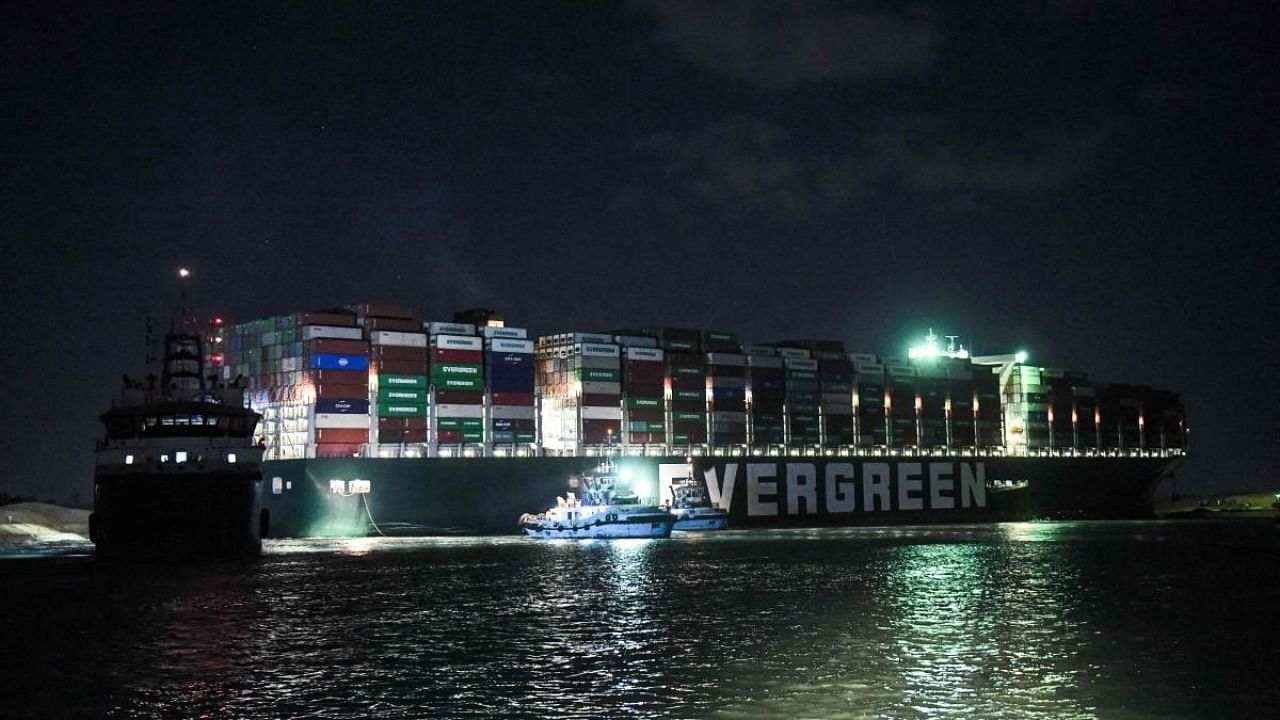 This picture taken late on March 27, 2021 shows a view of tugboats by the Panama-flagged MV 'Ever Given' container ship, which has been wedged diagonally across the span of the canal about six kilometres north of the Suez Canal's entrance by the Red Sea port city of Suez since March 23. Credit: AFP.