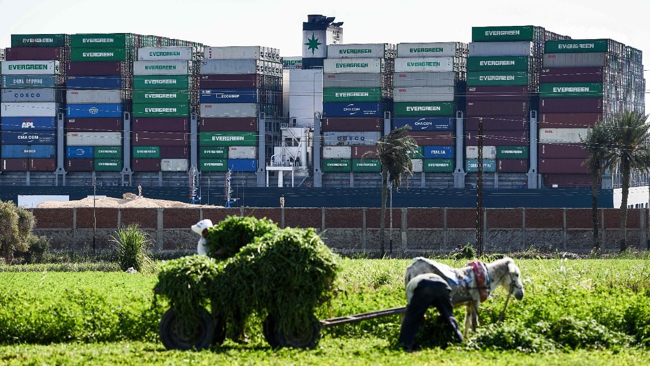 Farmers load a donkey-drawn cart with produce (foreground) as Egyptian army soldiers stand on guard (background) near the grounded Panama-flagged container ship MV 'Ever Given'. Credit: AFP Photo