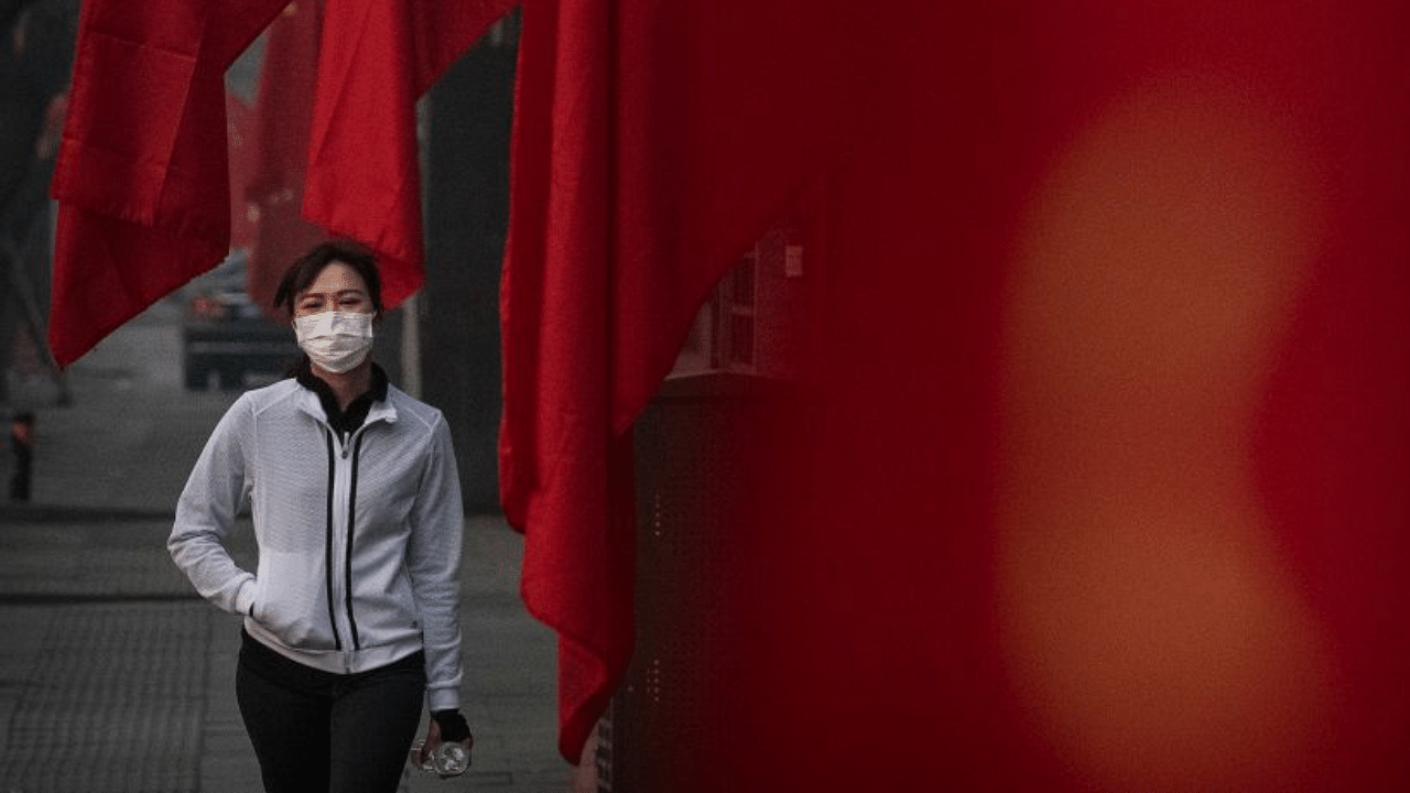 A woman wears a protective mask as she walks by Chinese flags in a street during the Chinese New Year and Spring Festival holiday on January 28, 2020 in Beijing, China. Credit: Getty Images