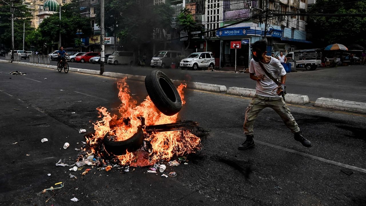 A protester throws a tyre to a burning makeshift barricade during a protest against the military coup, in Yangon on March 30, 2021. Credit: AFP Photo