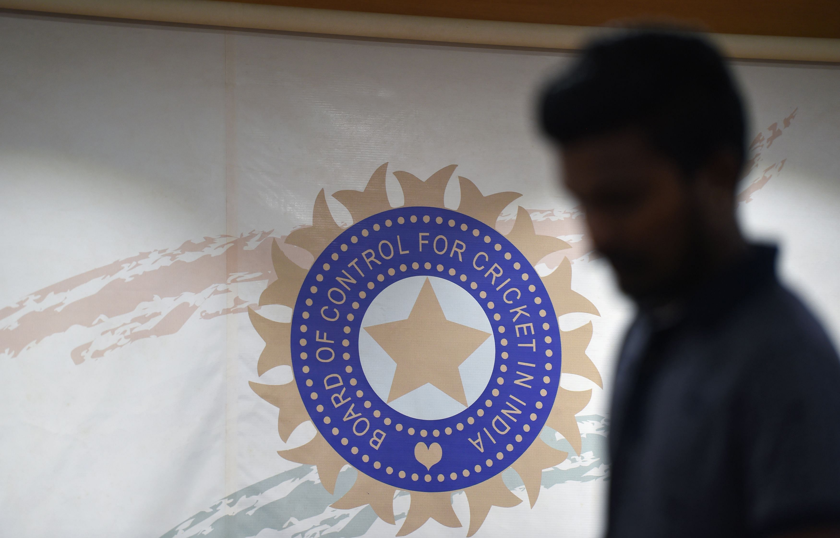 A man walks in front of the logo for the Board of Control for Cricket in India (BCCI). Credit: AFP File Photo