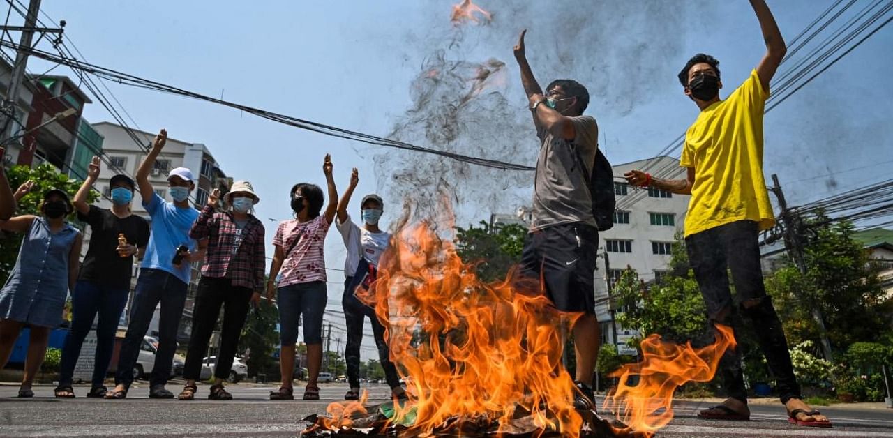 Protesters make the three-finger salute as copies of the 2008 constitution are burnt during a demonstration against the military coup in Yangon. Credit: AFP Photo