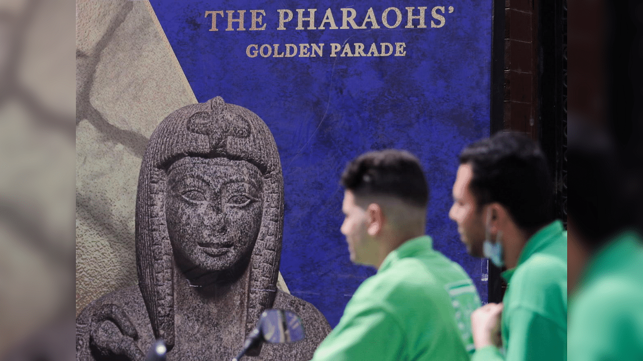 Men pass in front of poster for pharaohs golden parade after the renovation of Tahrir Square for transferring 22 mummies from the Egyptian Museum in Tahrir to the National Museum of Egyptian Civilization in Fustat, amidst the outbreak of coronavirus disease (COVID-19), in Cairo, Egypt, April 1, 2021. Credit: Reuters