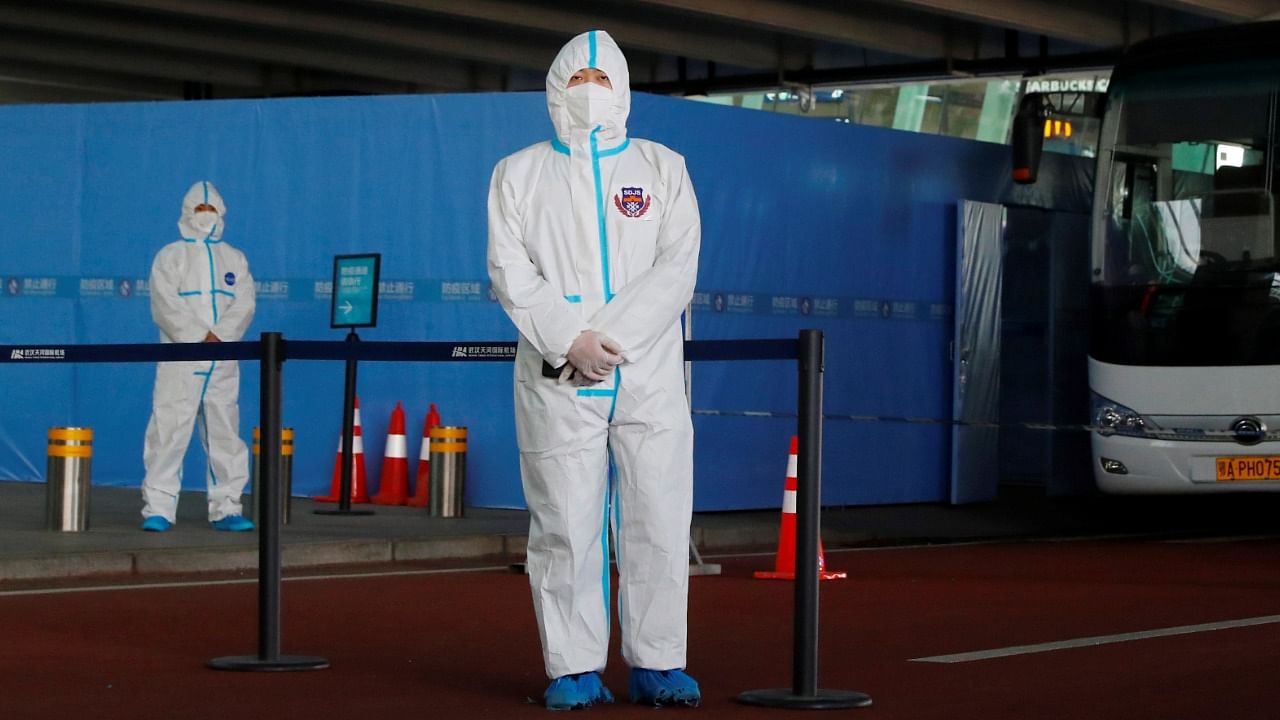 Staff members in protective suits stand guard next to a bus before the expected arrival of a World Health Organization (WHO) team in Wuhan. Credit: Reuters File Photo