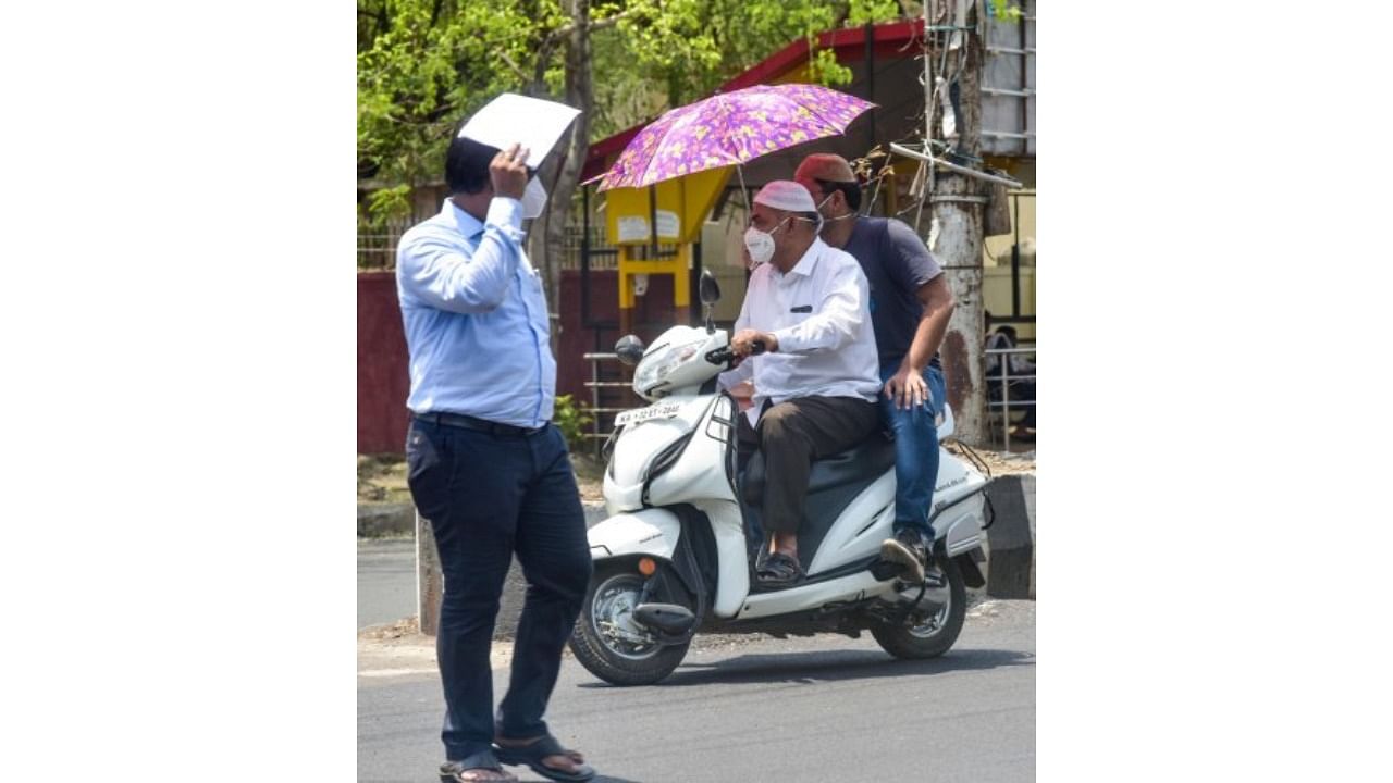 A scooter rider, his pillion use umbrella to beat the heat in the city. Credit: DH File Photo