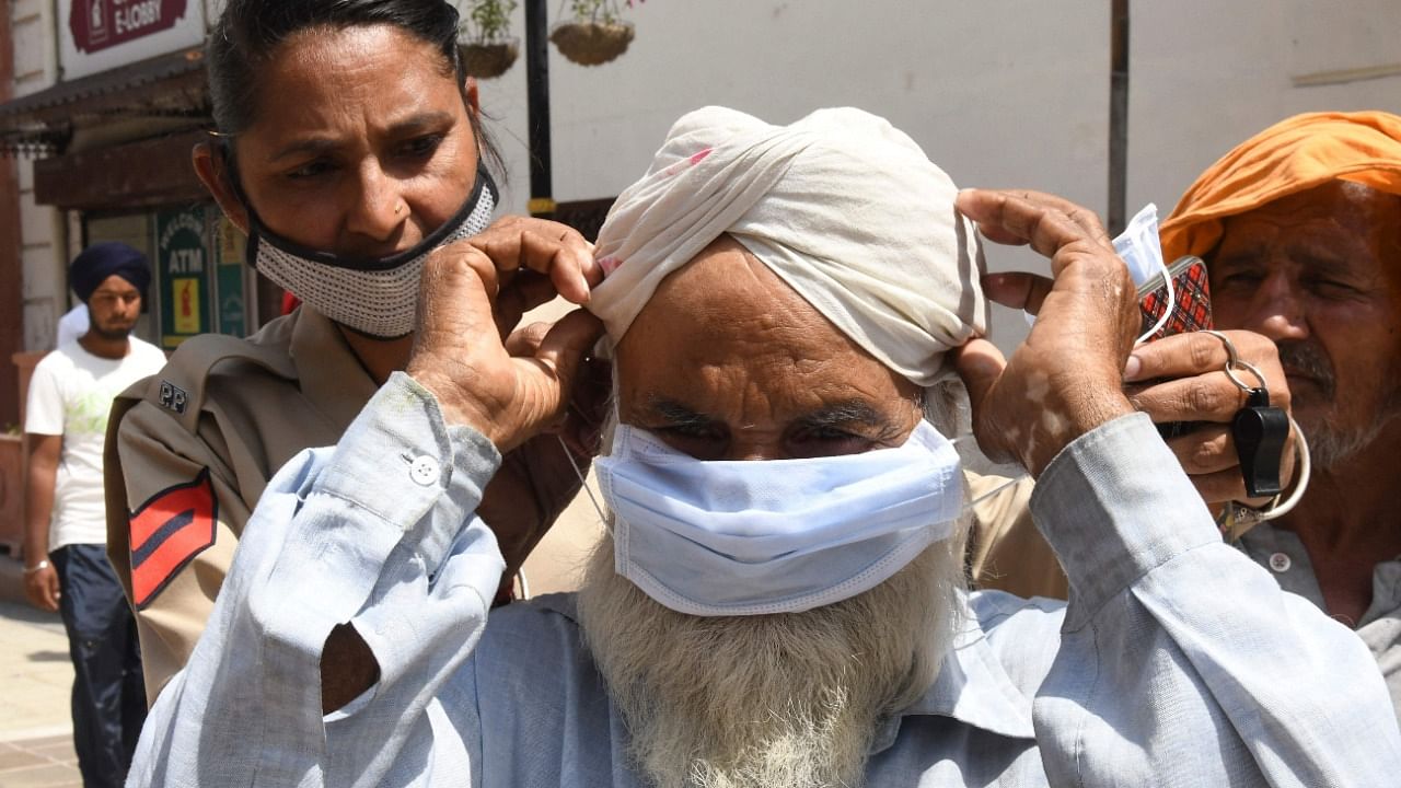 A police personnel (L) ties a mask on the face of a man during an awareness campaign against the spread of the Covid-19 coronavirus, in Amritsar. Credit: PTI.