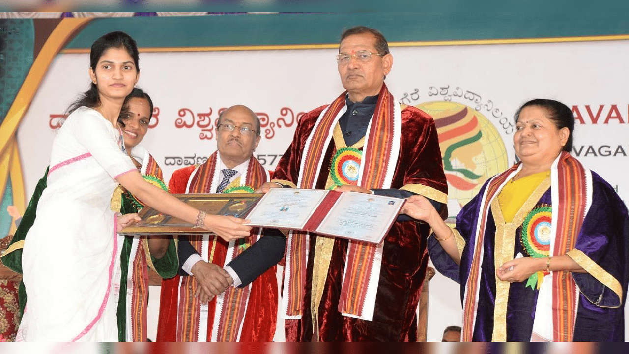Davangere University Vice-chancellor Sharanappa V Halase presents gold medals and certificate to Nisarga K P, who secured the first rank in MA (English) even when she had epilepsy during examinations last year, at the 8th convocation in Davangere on Thursday. University Registrar (Evaluation) H S Anitha, Academy for Creative Teaching Chairman Gururaj Karajagi, and Registrar Gayathri Devaraj are seen. Credit: DH Photo