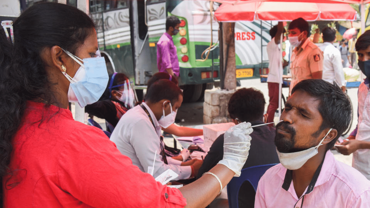 A health volunteer collects nasal swab sample at a free Covid-19 camp set up at Kalasipalya Bus Stand in Bengaluru on Friday. DH Photo/S K Dinesh