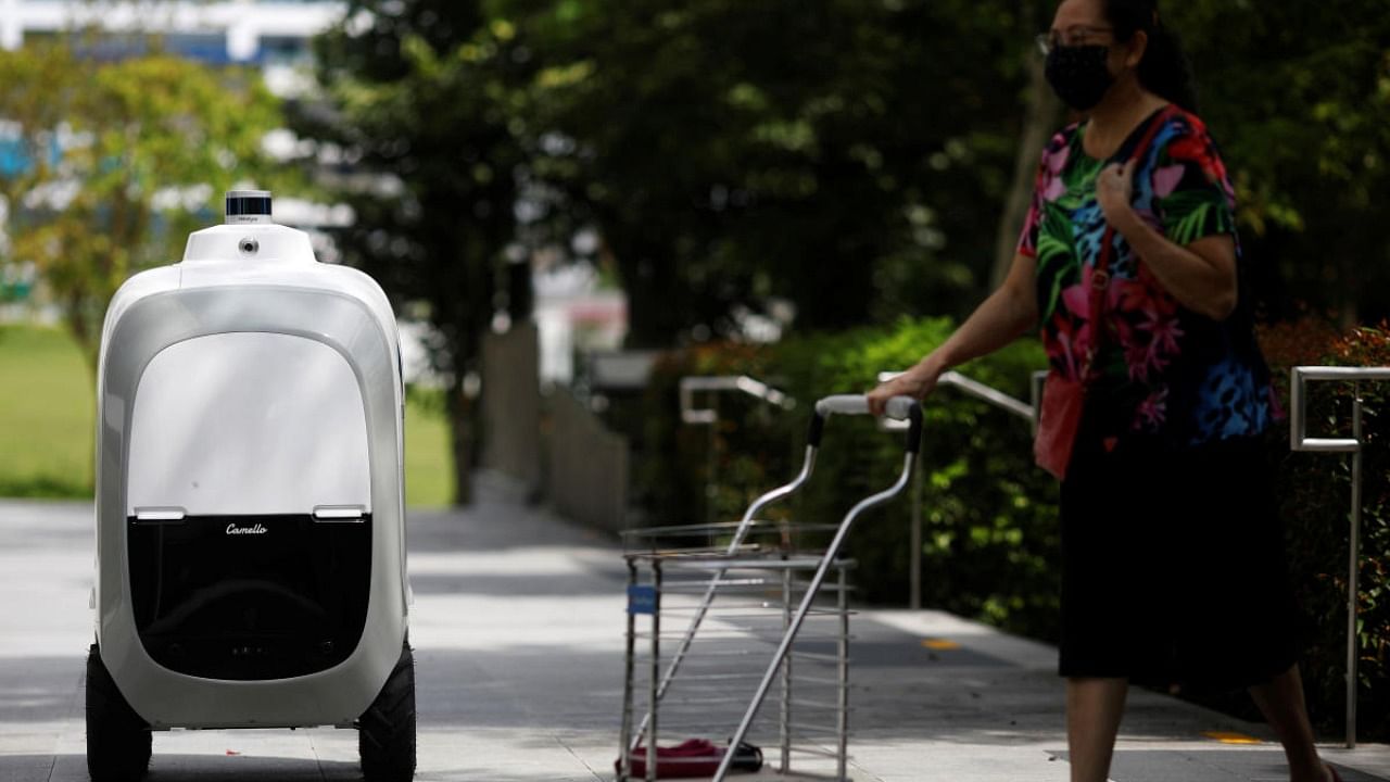 A woman pushes a trolley past Carmello, an autonomous grocery delivery robot, in Singapore. Credit: Reuters Photo