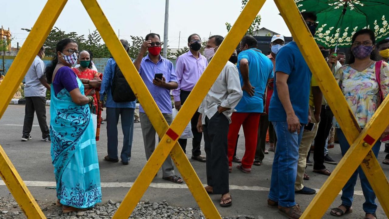 People stand behind a barrier outside a Covid-19 vaccination centre in Mumbai. Credit: AFP photo. 