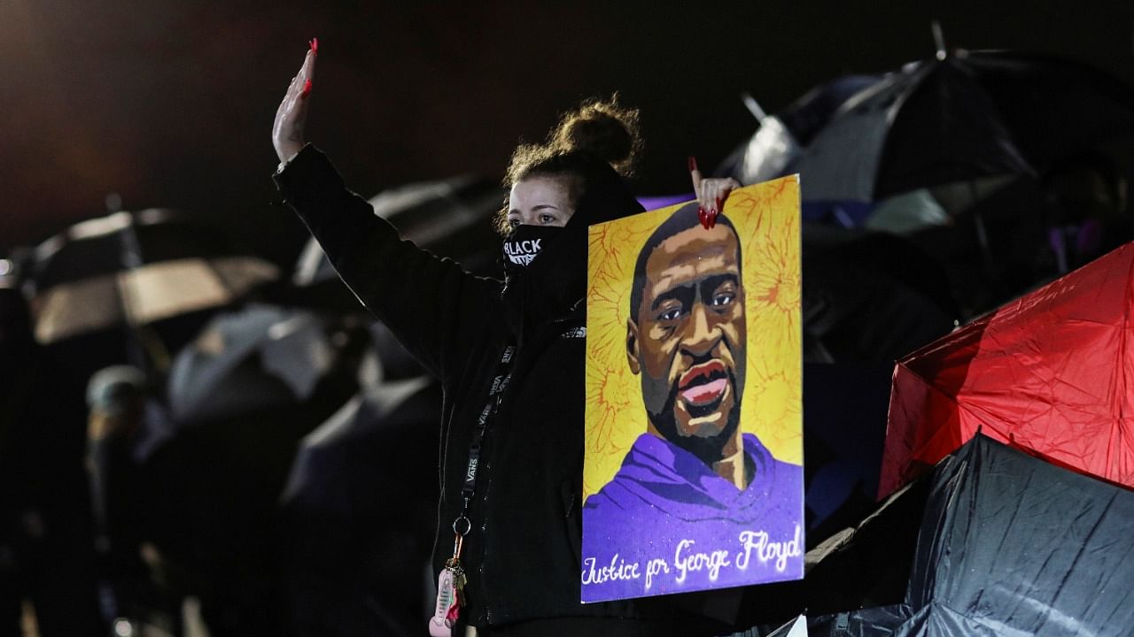A woman holding an image of George Floyd reacts while standing between the police and protesters chanting for Daunte Wright outside the Brooklyn Center Police Department, days after Wright was shot and killed by a police officer, in Brooklyn Center, Minnesota, US, April 14, 2021. Credit: Reuters Photo