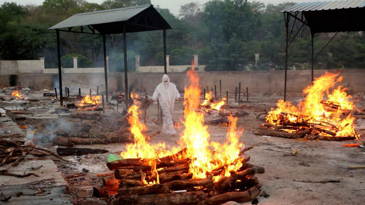 A worker, wearing PPE kit, performs cremation of Covid-19 victims, in Bhopal. Credit: PTI photo
