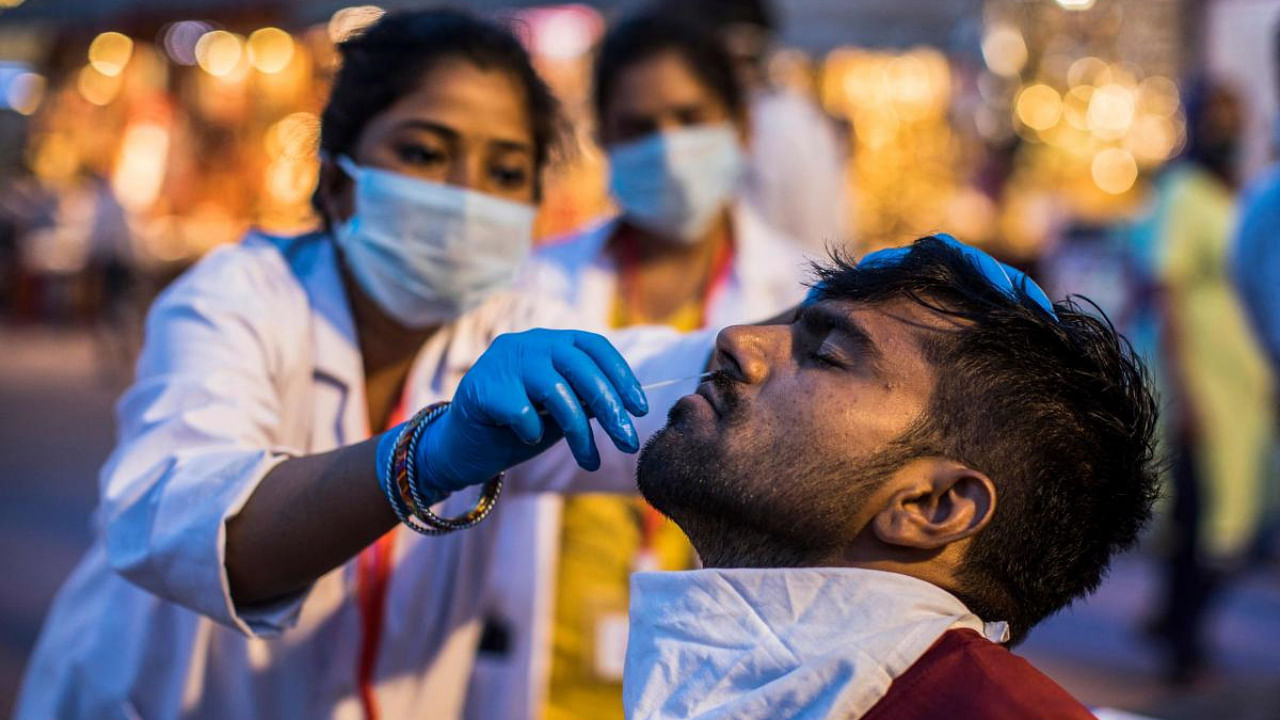 A health worker collects a nasal swab sample from a person to test for the coronavirus during the ongoing religious Kumbh Mela festival, in Haridwar. Credit: AFP photo. 