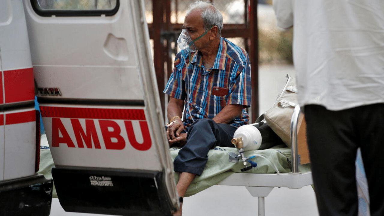 A patient wearing an oxygen mask sits on a bed as he is being shifted to a hospital for treatment, amidst the spread of the coronavirus disease in Ahmedabad. Credit: Reuters photo. 