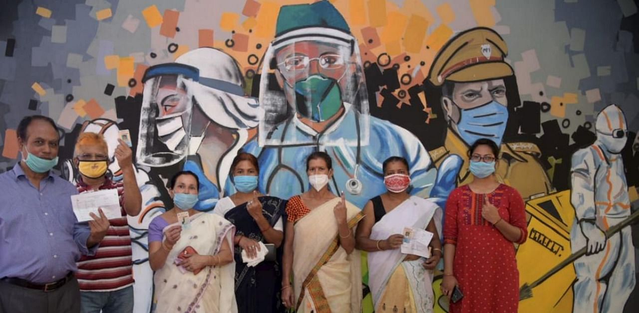  People pose for photographs in front of a wall art dedicated to Corona warriors after votes for Assembly polls, at a model polling Station in Guwahati. Credit: PTI Photo