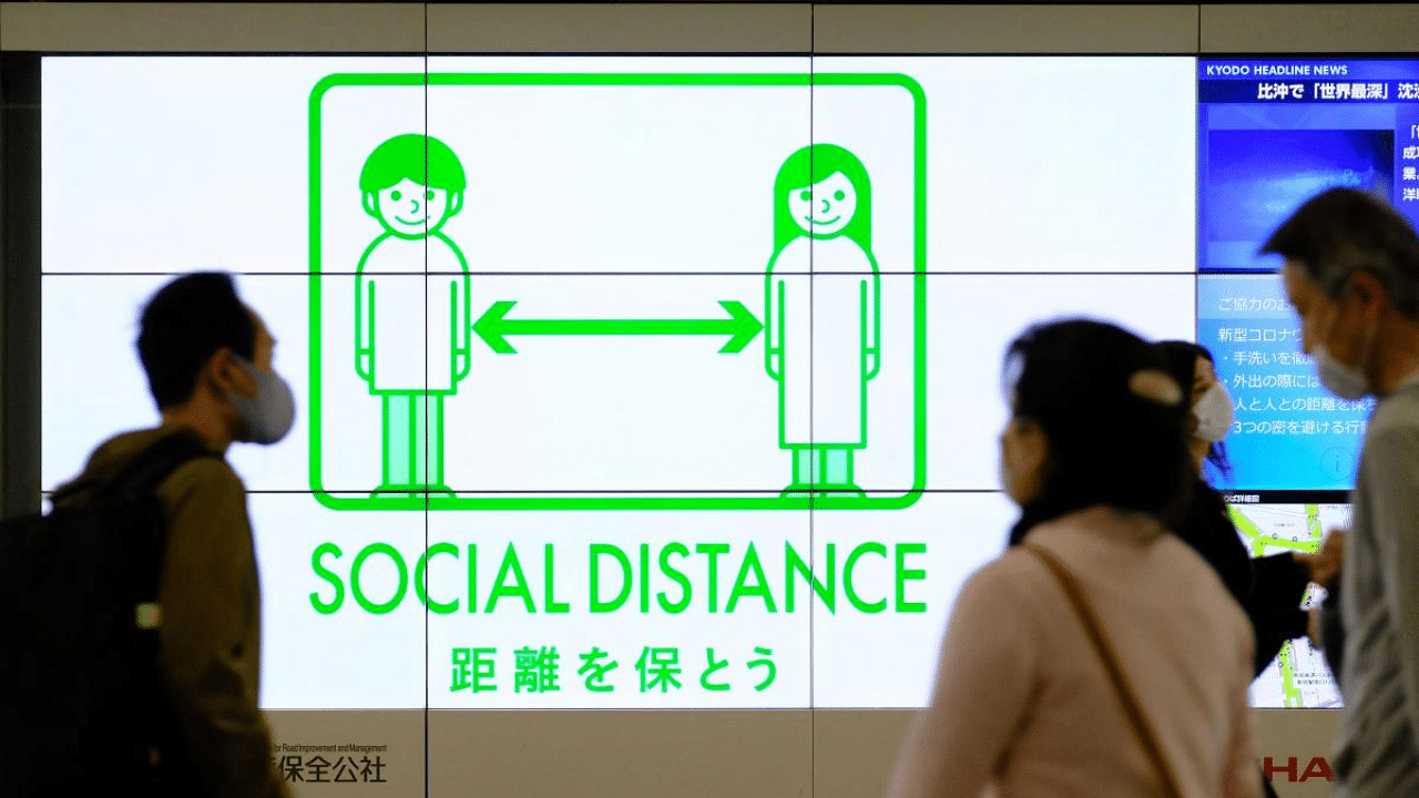 People wearing face masks walk past a public service display promoting social distancing at a concourse leading to the terminal station in Tokyo's Shinjuku district. Credit: AFP photo. 
