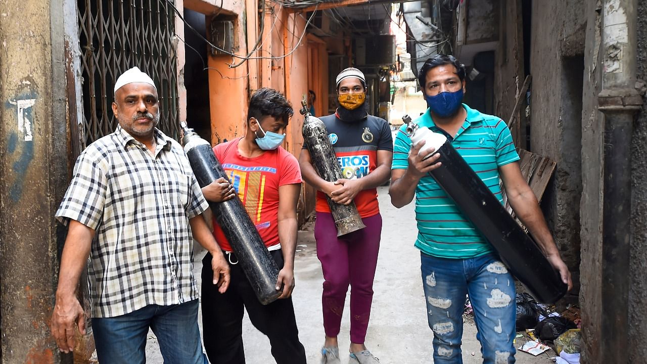 People carry empty oxygen cylinders for free refilling provided by Residence Welfare Association  of Turkman Gate. Credit: PTI Photo