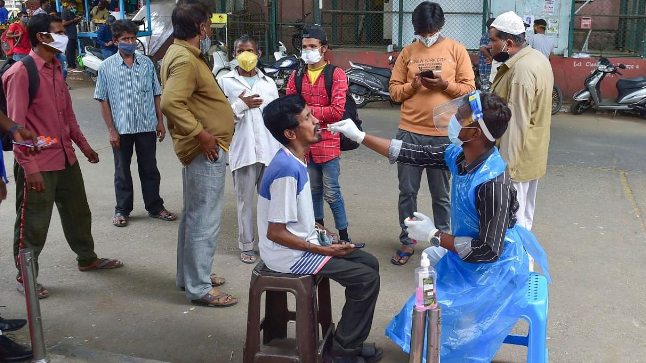 A medic collects samples for Covid-19 testing from a passenger, amid surge in coronavirus cases at City Railway Station in Bengaluru. Credit: PTI Photo