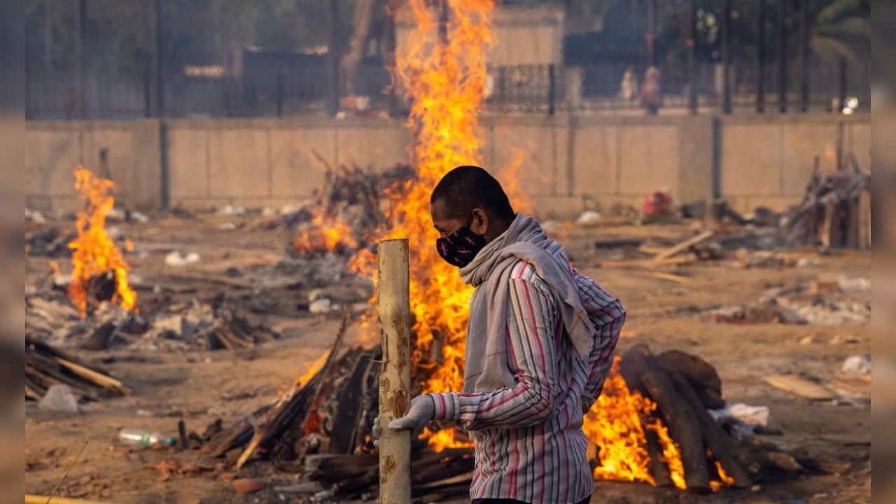 A man walks past burning funeral pyres of people, who died due to the coronavirus disease (Covid-19), at a crematorium ground in New Delhi. Credit: Reuters Photo