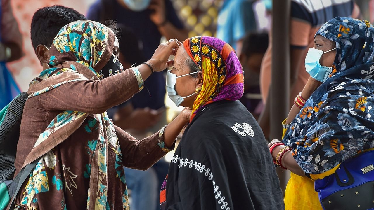A woman helps an old lady to wear face mask at Bengaluru City Railway Station amid surge in coronavirus cases, in Bengaluru, Wednesday, April 14, 2021. Credit: PTI Photo