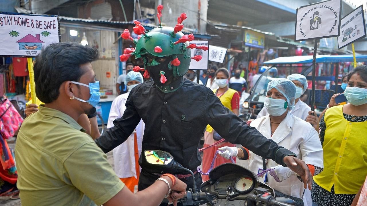 A man from a Non-governmental organisation (NGO) wearing an outfit resembling the Covid-19 coronavirus moves around a marketplace urging people to follow the safety protocols during an awareness drive held in Siliguri on April 25, 2021. Credit: AFP Photo