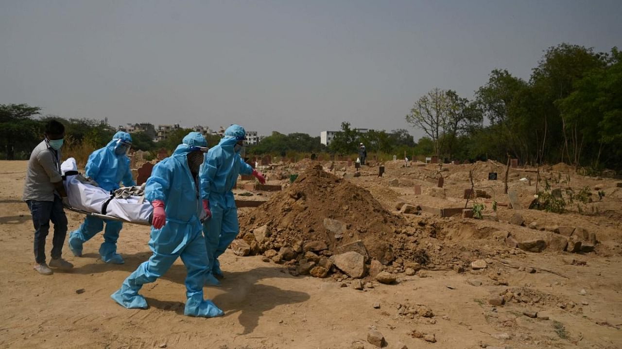 Relatives and friends put on personal protective equipment (PPE) suits before the burial of their loved one who died from the Covid-19 coronavirus, at a graveyard in New Delhi. Credit:  AFP Photo