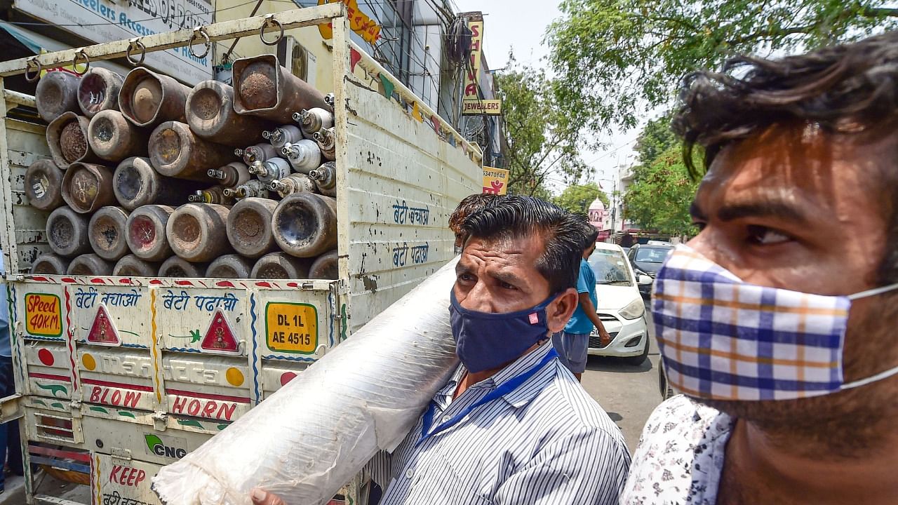 A family member of a Covid-19 patient carries a cylinder containing medical oxygen after refilling, as demand for the gas rises due to spike in coronavirus cases, in New Delhi, Saturday, May 1, 2021. Credit: PTI Photo