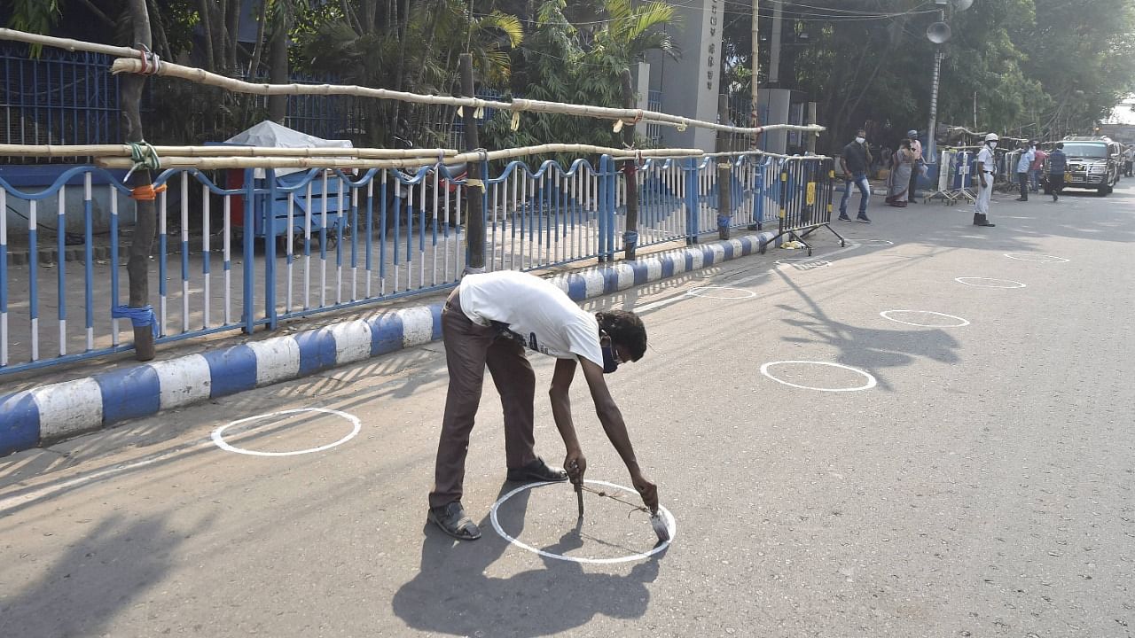 worker draws markers on the road to ensure social distancing as coronavirus cases spike across the country, outside Netaji Indoor Stadium on the eve of counting day of West Bengal Assembly Poll, in Kolkata, Saturday, May 1, 2021. Credit: PTI Photo