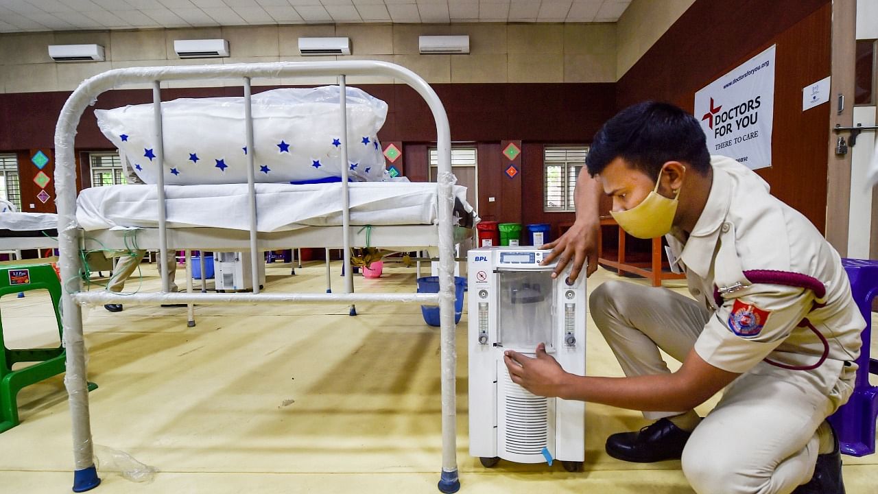 A volunteer prepares beds with oxygen concentrators and oxygen cylinders at a Covid Care Centre in New Delhi. Credit: PTI File Photo
