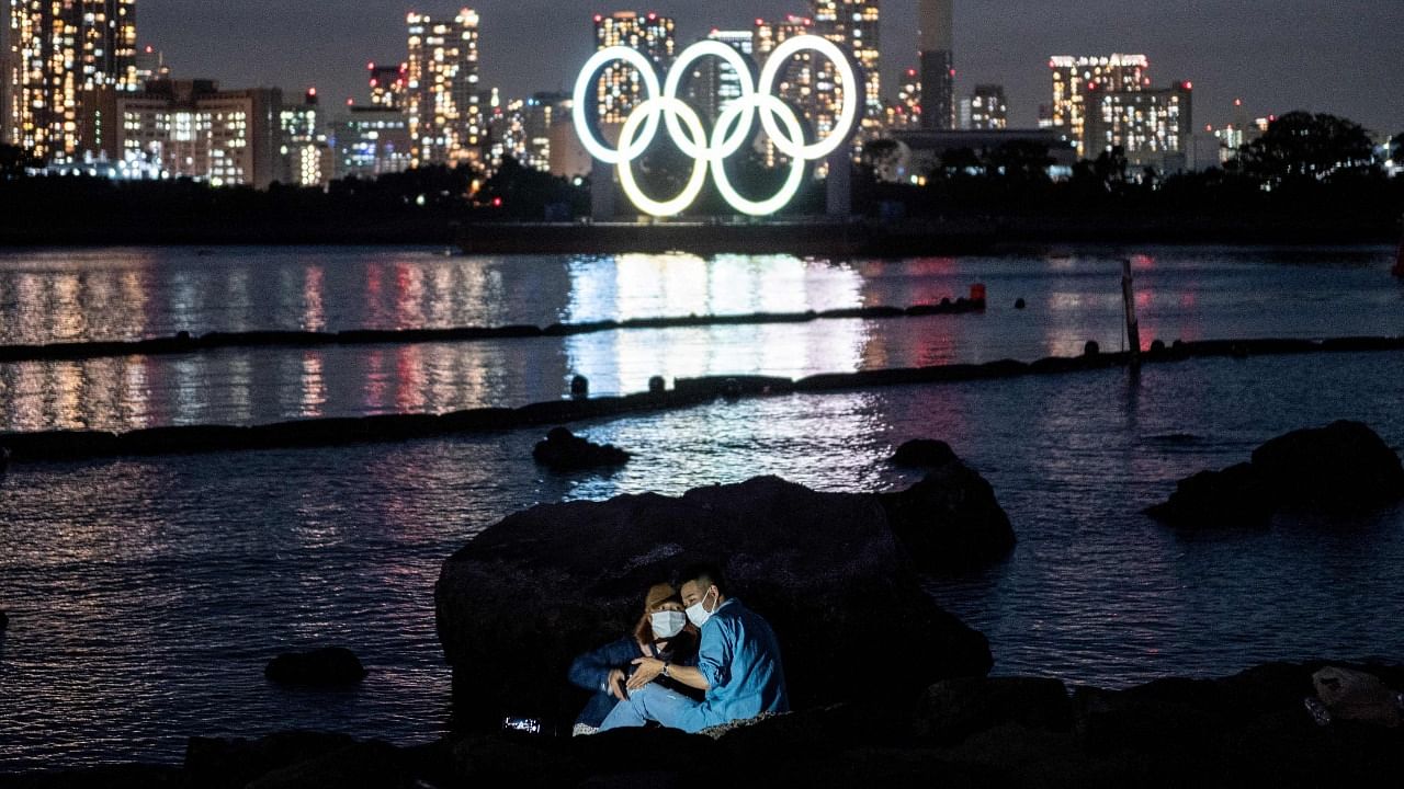 A couple pose for pictures before the lit Olympic rings at the Odaiba waterfront in Tokyo on May 6, 2021. Credit: AFP Photo